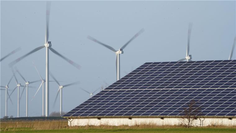 Windenergieanlagen stehen neben einer Halle mit Photovoltaik-Anlagen.