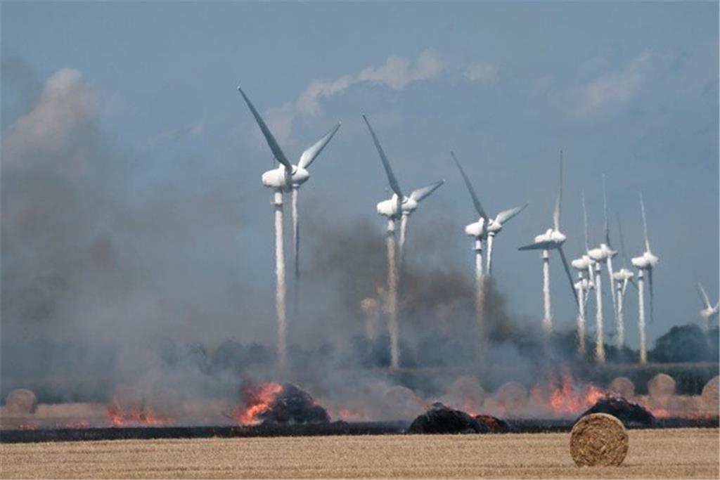 Windräder sind hinter den brennenden Strohballen zu erkennnen.