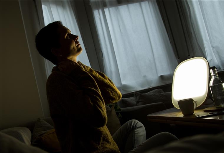 Eine Frau sitzt in der Dunkelheit vor einer Lampe. 