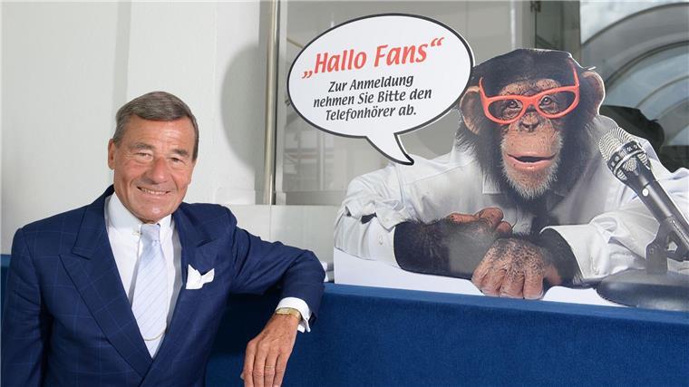 Wolfgang Grupp senior mit einem Werbeschild, auf dem der bekannte Werbe-Affe „Charly“ abgebildet ist.