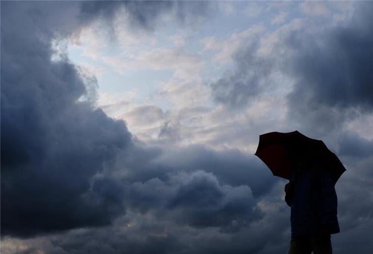 Wetter am Freitag: Regen und Unwetter erwartet ARCHIV - 12.07.2019, Nordrhein-Westfalen, Duisburg: Ein Mann geht mit einem Regenschirm vor aufziehenden dunklen Wolken spazieren. Nach ersten sonnigen Frühlingstagen schwenkt das Wetter in Nordrhein-Westfalen schon wieder um. Heftiger Starkregen, stürmische Böoen und kleinkörniger Hagel sind möglich. (zu dpa «Prognose: «Unwetter möglich» mit Starkregen, Sturm und Hagel in NRW») Foto: Martin Gerten/dpa +++ dpa-Bildfunk +++
