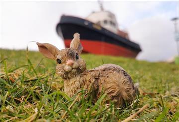 Ein Hasen-Modell sitzt im Gras vor einem an Land stehenden Museumsschlepper.