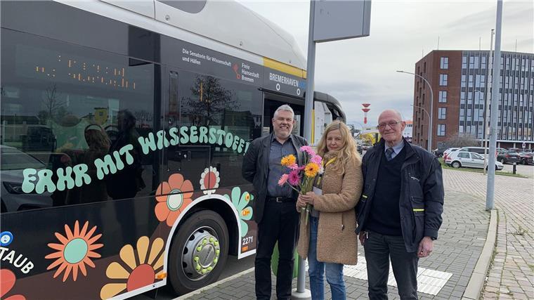 Zur Premierenfahrt des Wasserstoffbusses gibt es Blumen für die Fahrgäste. Jörg Fröhlich (Betriebsleiter Bremerhaven Bus), Imme Hüller (Marketing, Bremerhaven Bus) und Busfahrer Winfried Bethke (von links) freuen sich auf Passagiere.