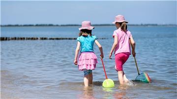 Zwei Mädchen spielen bei sonnigem Wetter mit ihren Keschern im flachen Wasser der Nordsee am Strand.