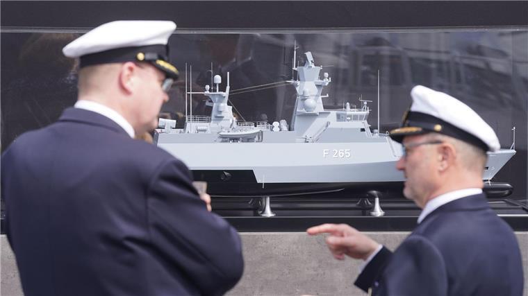 Zwei Marinemitglieder stehen vor einem Modell vor der Taufzeromonie der Korvette F 266 „Emden“ auf dem Werftgelände von Blohm+Voss im Hafen.