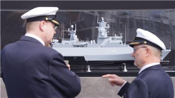 Zwei Marinemitglieder stehen vor einem Modell vor der Taufzeromonie der Korvette F 266 „Emden“ auf dem Werftgelände von Blohm+Voss im Hafen.
