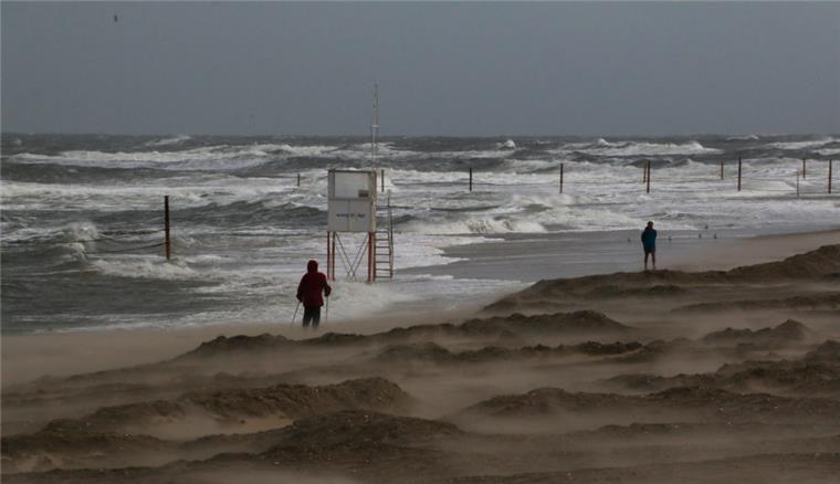 Sturm trifft in der Nacht auf die Nordseeküste Zwei Menschen wandern bei stürmischem Wind am Strand entlang.