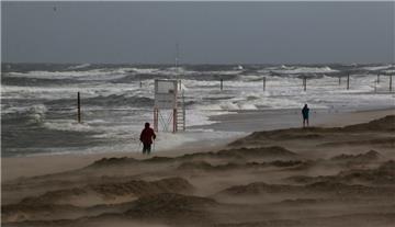 Zwei Menschen wandern bei stürmischem Wind am Strand entlang.