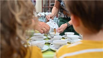 Zwei Mitarbeiter des Teemuseums schenken unter den Augen zweier junger Gästen, Tee nach Ostfriesischer-Art ein.