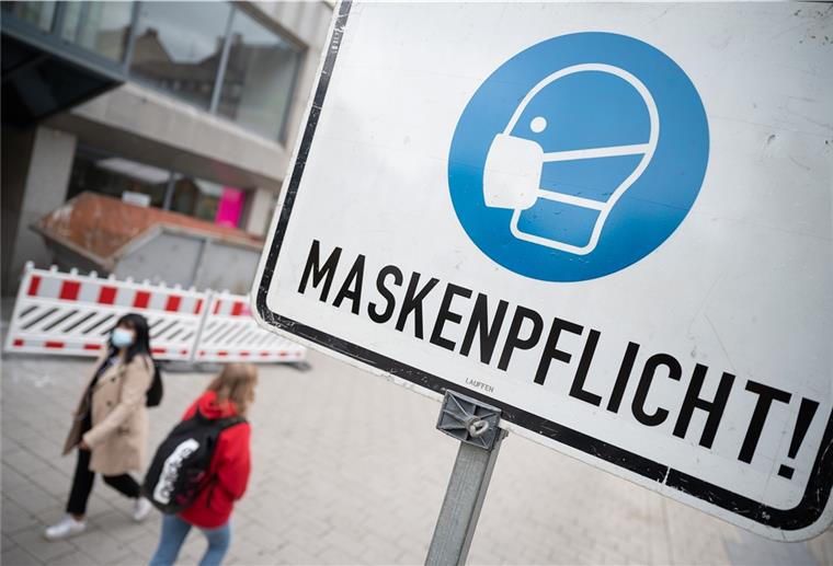 Zwei Passantinnen gehen in einer Fußgängerzone hinter einem Schild vorbei, auf dem „Maskenpflicht“ steht.
