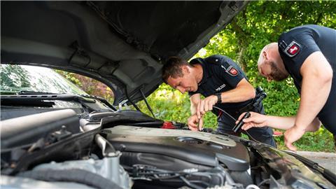 Zwei Polizisten der Arbeitsgruppe „Auto-Poser“ schauen in den Motorraum eines Fahrzeuges.