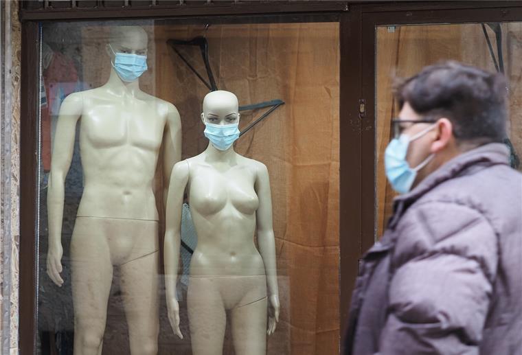Zwei Schaufensterpuppen mit Maske stehen in einem Schaufenste.