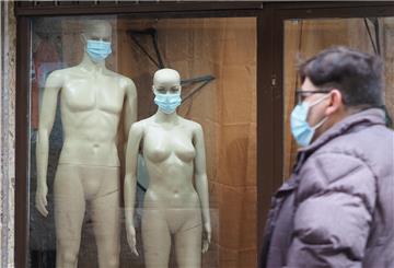 Zwei Schaufensterpuppen mit Maske stehen in einem Schaufenste.