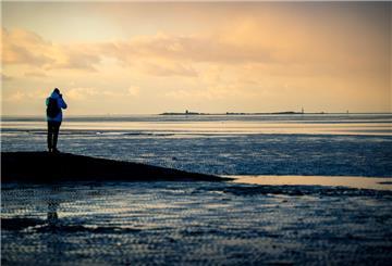 Ein Spaziergänger steht im Watt vor Cuxhaven und fotografiert die Insel Neuwerk.